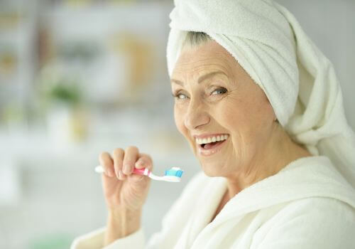 Older woman with hair wrapped in a towel brushing her teeth