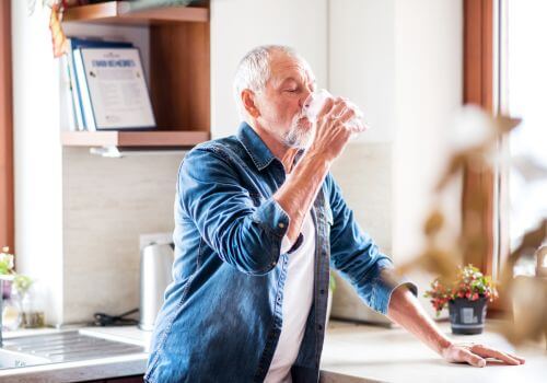 Senior man standing in kitchen drinking a glass of water