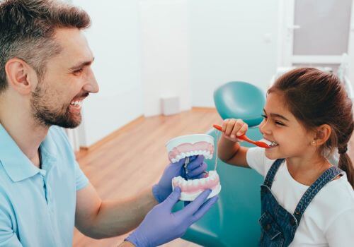 Young girl learning how to brush her teeth from her dentist.
