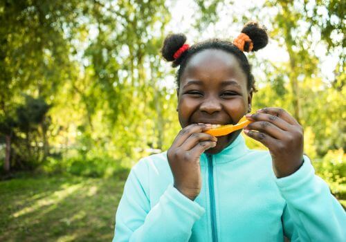 Young girl eating an orange slice outside