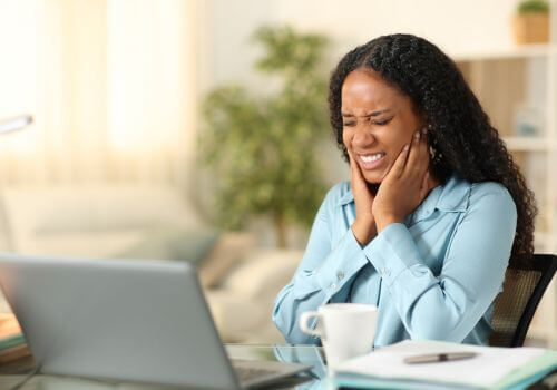 Young woman working at laptop suffering from TMJ pain