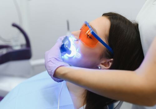 Young woman recieving professional teeth whitening at the dentist.