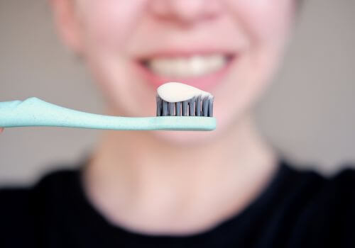 Woman holding up soft bristled toothbrush with desensitizing toothpaste on it for sensitive teeth