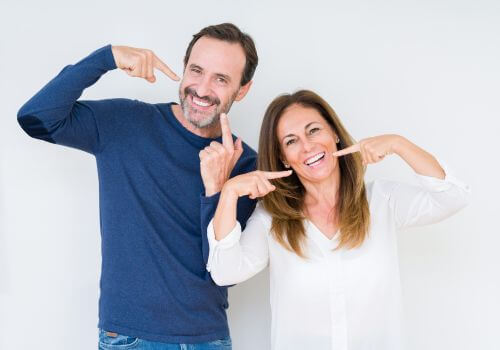 Wife and husband smiling, showing their cosmetic dentistry makeovers. Smile makeover after picture.