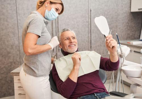 Older man smiling and using a mirror at the dentists office after gum contouring