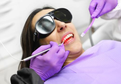 Dentist using modern diode dental laser on female patient